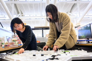 Two people in a studio touch a model of an urban landscape.