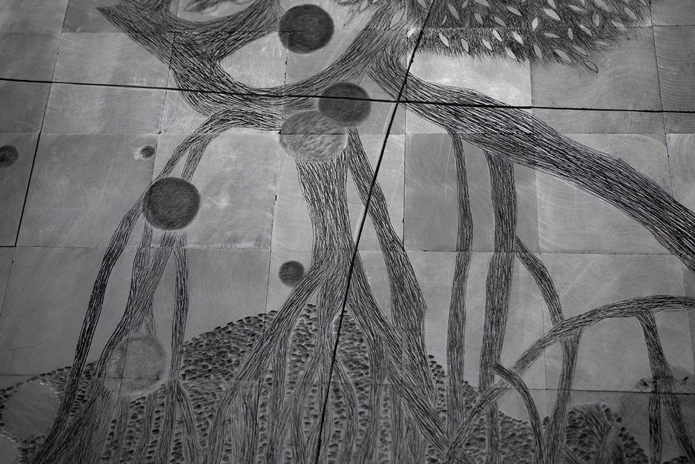 A black-and-white photograph showing an abstract composition resembling a tree's root system etched into metal panels that are arranged in a grid. 