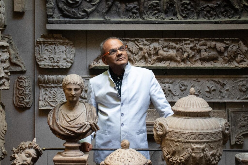 A photograph of Hanif Kara standing in a museum surrounded by Classical sculptures, vases, and friezes.