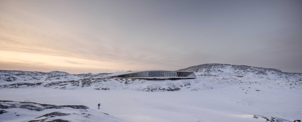 narrow and long glass building in a snowy mountainous landscape at sunet