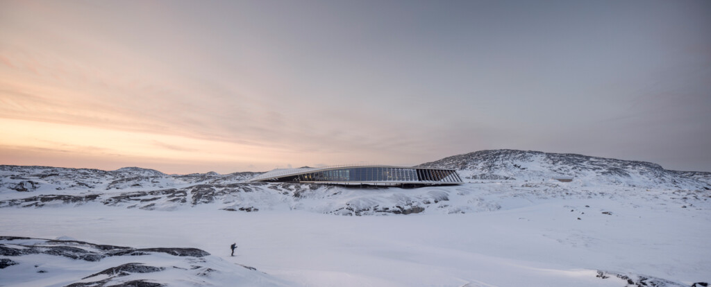 A view of a contemporary structure with a curving roof and many windows set in a frozen landscape.